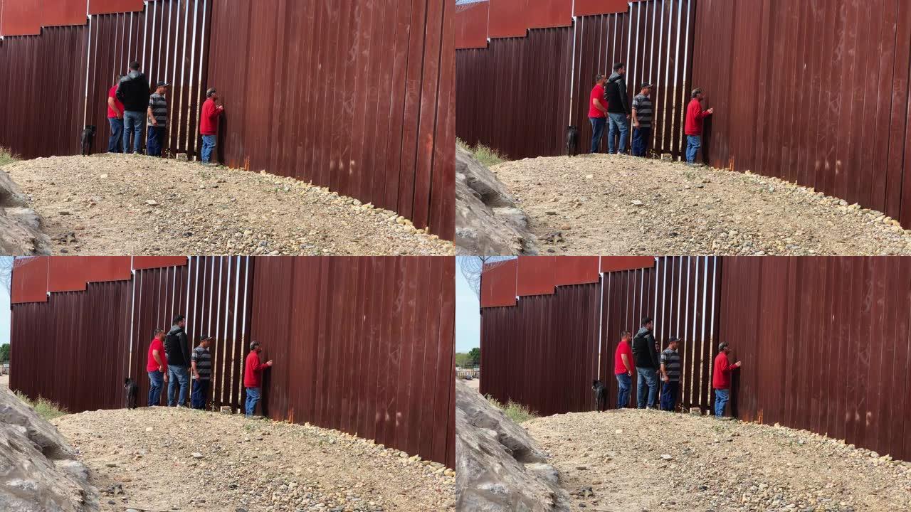 一组四名墨西哥人透过边境围栏望向美国一侧的国际边境墙