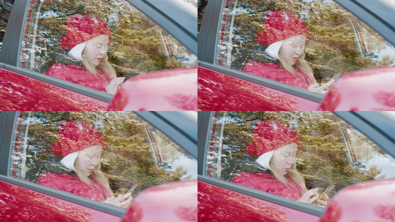 年轻女子在红色车内使用手机。戴着红色帽子和夹克的无忧无虑的女孩在乘客座位上的车内打字智能手机，户外视