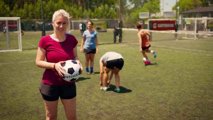 女足球运动员站在足球场上，抱着球