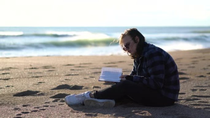 英俊的男人坐在沙滩上看书