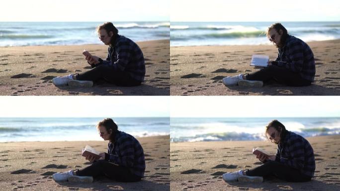 英俊的男人坐在沙滩上看书