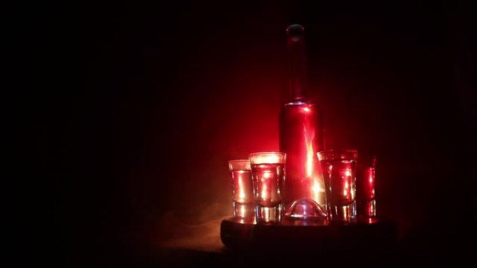 一个漂亮的玻璃瓶和伏特加站在一个带眼镜的木桌上。戏剧性的色调雾状背景与光线。选择性聚焦。俱乐部饮料概