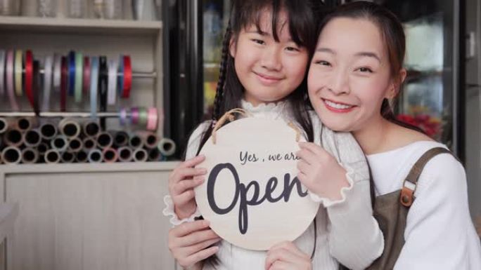 小女孩和她的母亲在花店举着开放标志。创业商业概念。