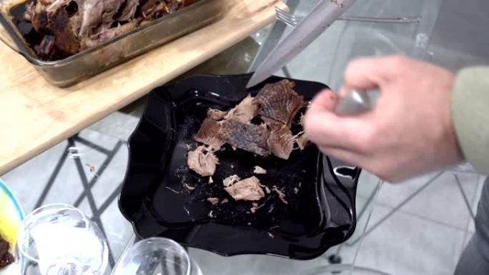 一名男子从厨房的黑盘中切出一块热炸鸭肉，并将其放在盘子上。家庭庆祝。特写。从顶部看。不露面。4K