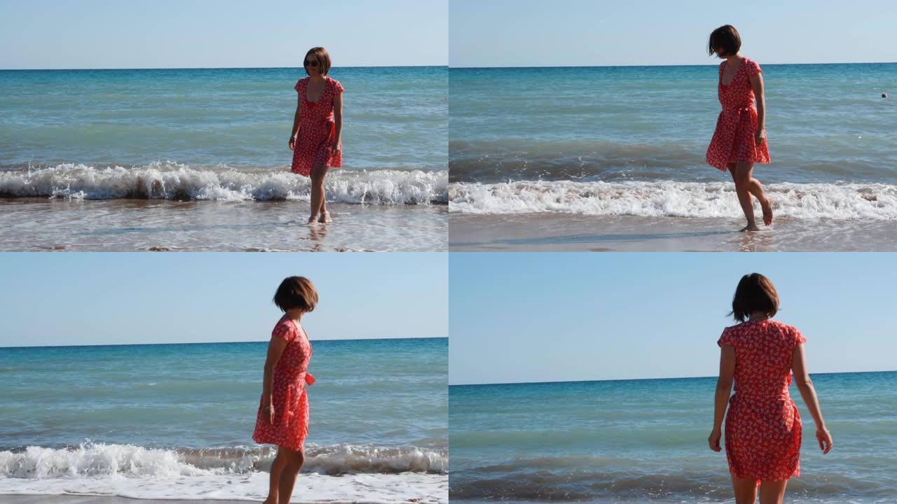穿着红色短裙的黑发高加索女孩在海滩散步。美丽的女孩在沙滩上玩得开心，微笑着。年轻迷人的女孩在海边放松
