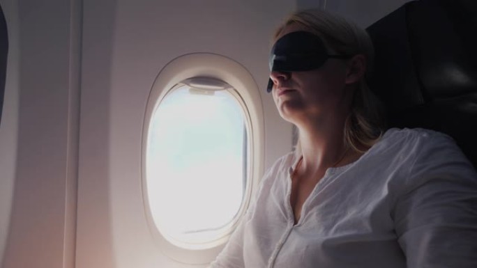 一名年轻女子眼睛里缠着深色绷带，睡在客机的机舱里。舒适旅行