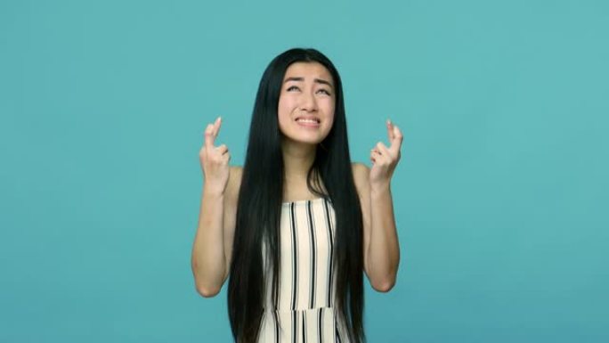 年轻的亚洲女性，留着长长的直发，手指交叉，示意好运，希望愿望成真