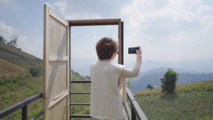 美丽的女孩用智能手机自拍的肖像，拿着屏幕对着相机。在背景风景秀丽的青山山景
