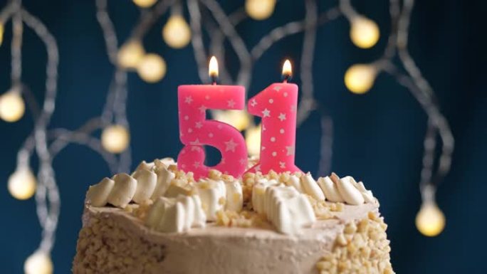 蓝色背景上有51号粉色蜡烛的生日蛋糕。蜡烛吹灭了。慢动作和特写视图