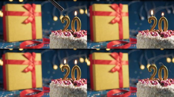 白色生日蛋糕20号点火器燃烧的金色蜡烛，蓝色背景带灯和用红丝带捆绑的礼物黄色盒子。特写
