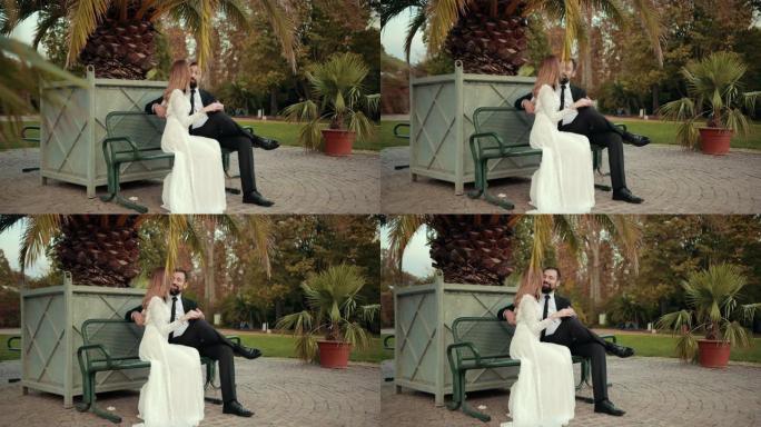 恋爱中的新婚夫妇坐在大棕榈树下的长凳上