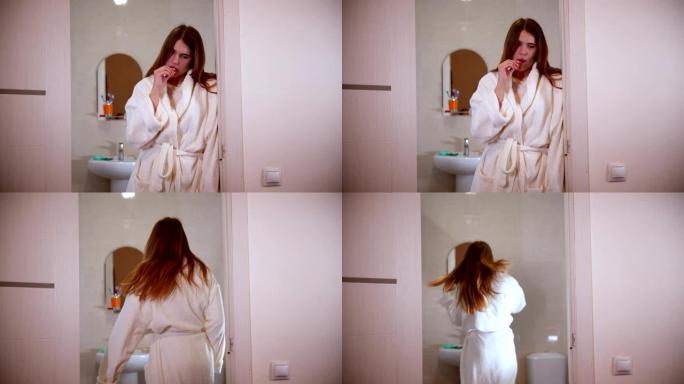 一名年轻女子早上穿着浴袍站在门口刷牙