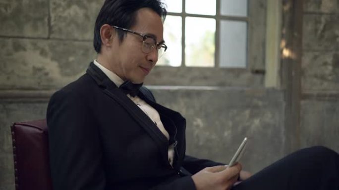 坐在红色椅子上的亚洲新郎使用智能手机在工作室里微笑着快乐。手持镜头。现实生活
