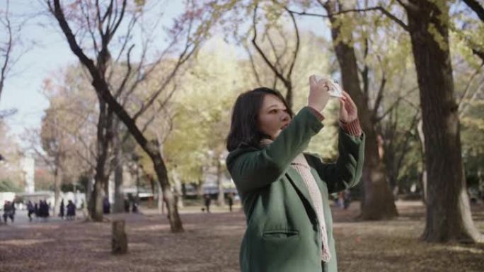 女人在秋天拍摄智能手机照片。