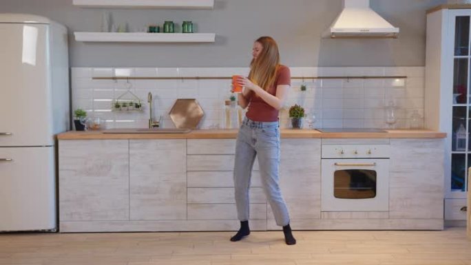 长发开朗的女人手持橙色咖啡在厨房跳舞