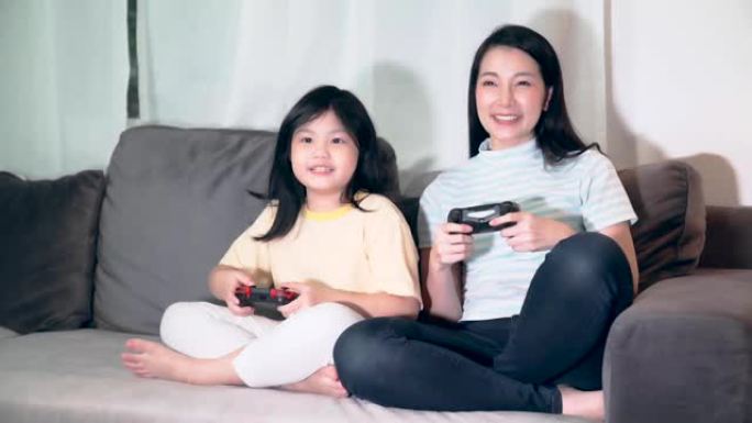 幸福亚洲家庭一起玩游戏机妈妈和女儿带着快乐的乐趣退出享受沙发家庭背景下的夜间活动