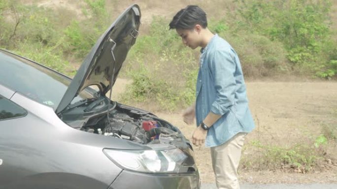 亚洲年轻不快乐的人在乡村道路上的敞篷抛锚汽车前检查损坏的汽车发动机，等待道路援助服务。旅途中的破车在