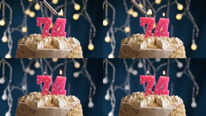 蓝色背景上有74号粉色蜡烛的生日蛋糕。蜡烛着火了。慢动作和特写视图