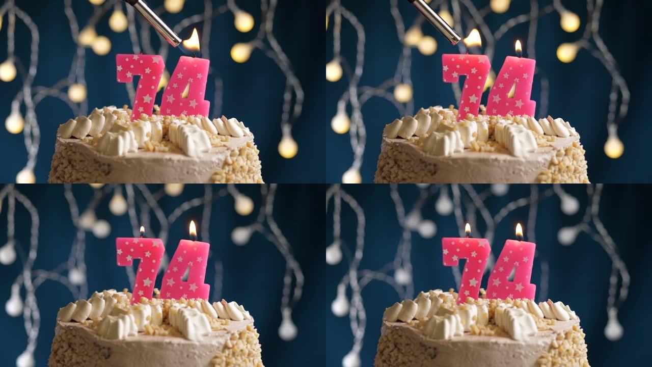 蓝色背景上有74号粉色蜡烛的生日蛋糕。蜡烛着火了。慢动作和特写视图