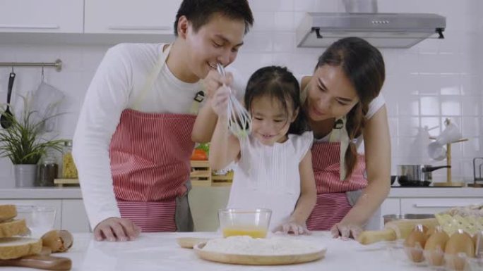 亚洲家庭，父亲和母亲在教女儿学做面包，女儿玩得很开心