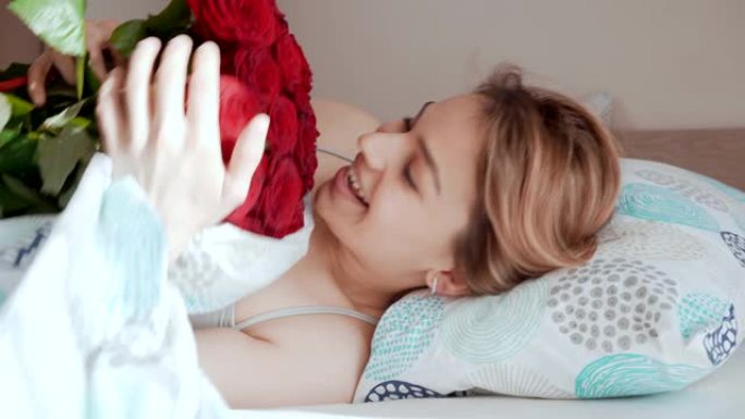 美丽的年轻女子醒来，收到玫瑰花束。床上迷人的女孩很高兴收到礼物。浪漫的概念。