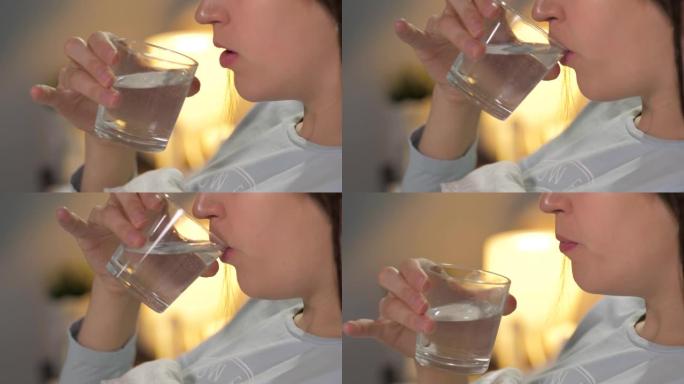 女孩睡前用透明玻璃喝水。特写