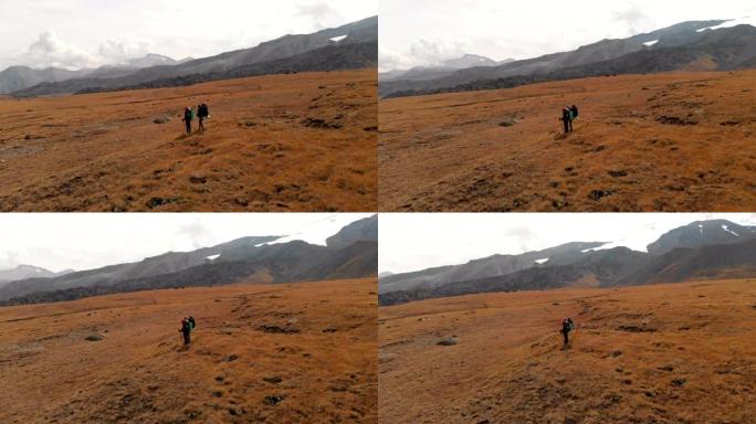 一对旅行者的鸟瞰图男女戴着帽子和墨镜的大背包站在被史诗般的山脉环绕的高山高原上