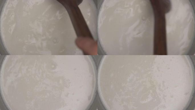 锅中沸腾的热泡沫牛奶的俯视图。牛奶与木勺混合。烹饪食物概念。特写。从上方观看。