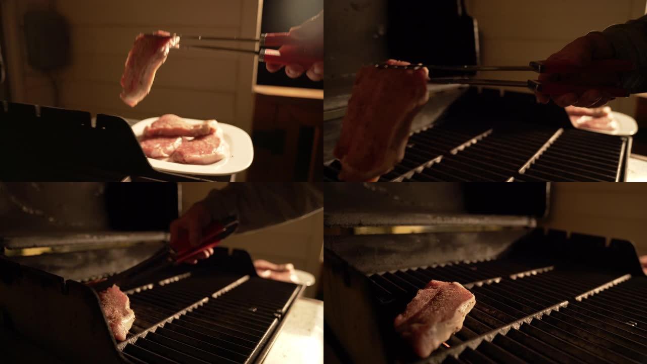 慢动作成人高加索人的手在户外晚上用烤肉钳将调味的、未煮熟的、去骨的里脊肉猪排放在烤架上，被天井灯照亮