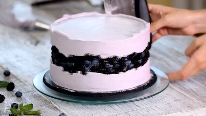 糖果用锅铲在饼干蛋糕上抚平紫色奶油。自制糕点的概念，烹饪蛋糕