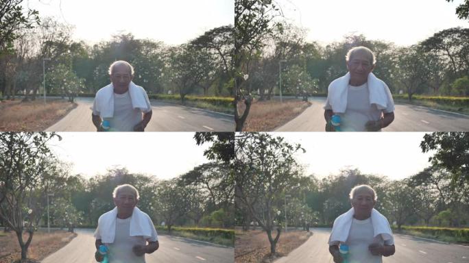 亚洲老人微笑着看着相机，在傍晚有阳光的公园里奔跑。健康生活方式和运动理念。慢动作