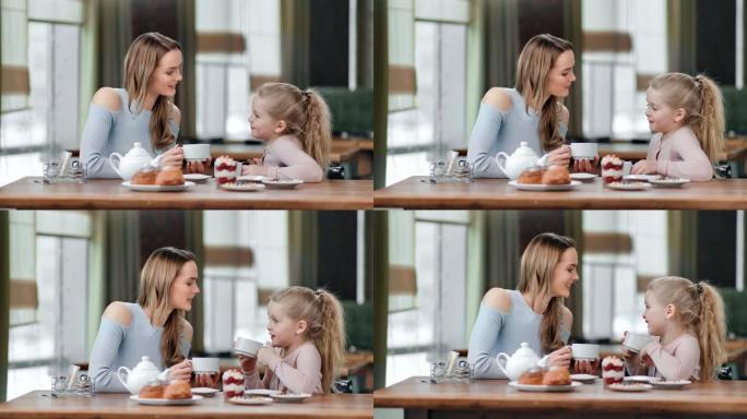 有爱心的年轻母亲和可爱的女儿在咖啡馆喝茶。红色相机上的中等镜头