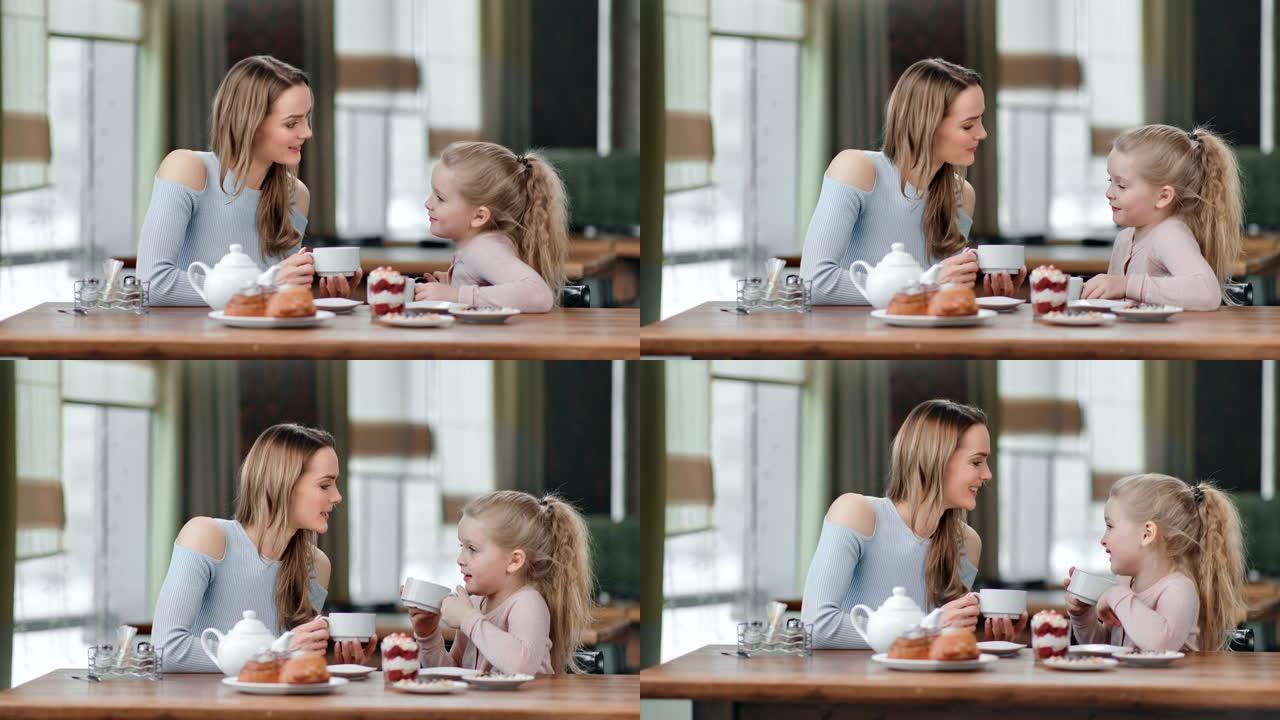 有爱心的年轻母亲和可爱的女儿在咖啡馆喝茶。红色相机上的中等镜头
