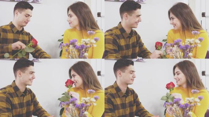 可爱的夫妇是交流和坐在咖啡馆里。男孩给他的女朋友一朵红玫瑰。她在吻他。4K。