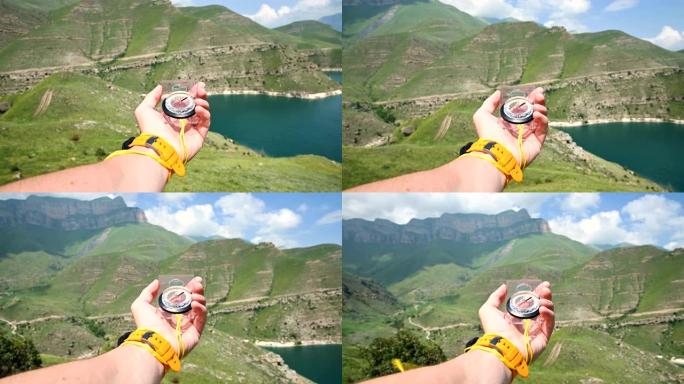 手持塑料磁性罗盘的男性手的第一人称视角在侧面旋转，并在山的背景中寻找正确的方向。定向运动的概念