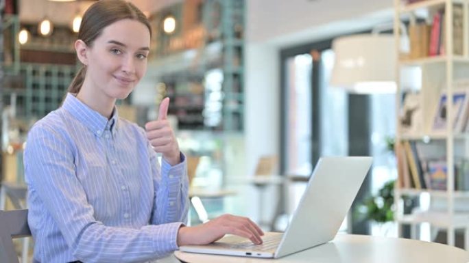 年轻的女商人在咖啡馆里使用笔记本电脑竖起大拇指