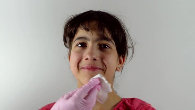 女性双手用杀菌餐巾摩擦女孩的脸