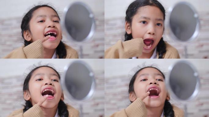 亚洲小女孩照镜子，检查她的嘴是否断了牙齿，带着快乐的情感，为牙齿和保健理念，选择焦点浅景深