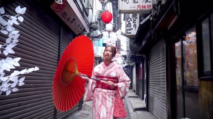 4k快乐年轻美丽的亚洲女子穿着传统的日本和服连衣裙，拿着红色纸伞微笑着走在街上，日本东京市新宿地区