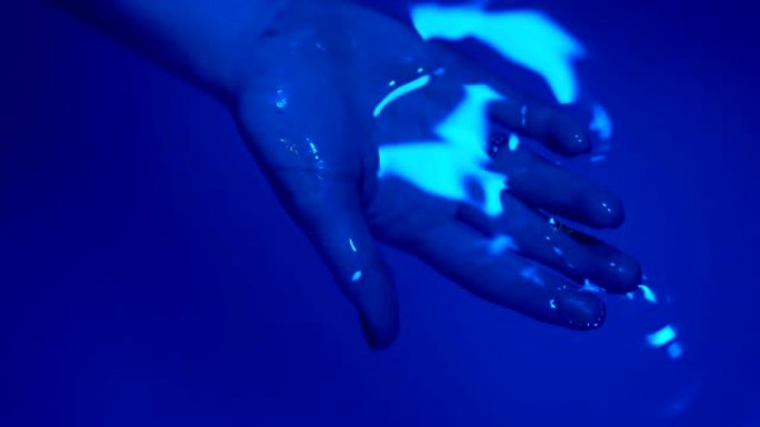 放松概念。一个年轻女子的手被握在水疗盆或水池的水面上，里面有海盐。超蓝镜头
