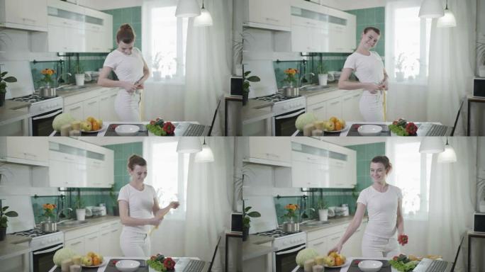 快乐的女人在成功节食后用厘米胶带测量她的腰部，然后他手里拿着苹果摘胡椒，在厨房里摆姿势拍照