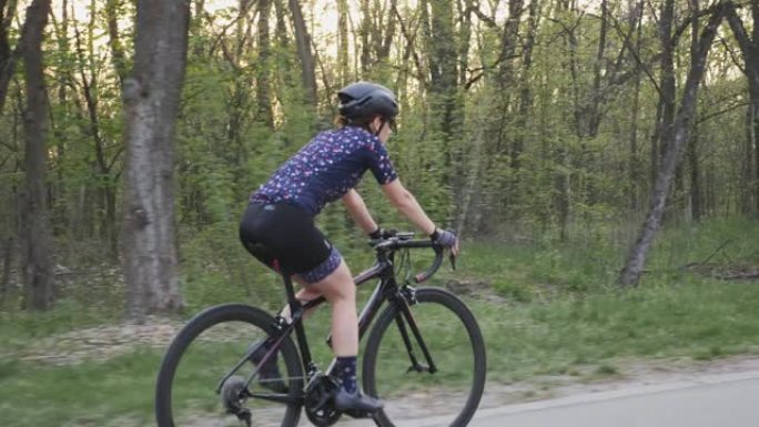 在公园的日落时分骑自行车的女骑车人。遵循侧视图。自行车和铁人三项概念。慢动作