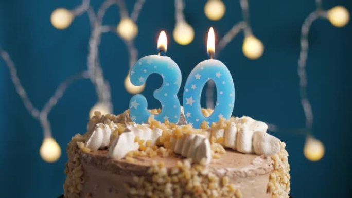蓝色背景上有30号蜡烛的生日蛋糕。蜡烛吹灭了。慢动作和特写视图