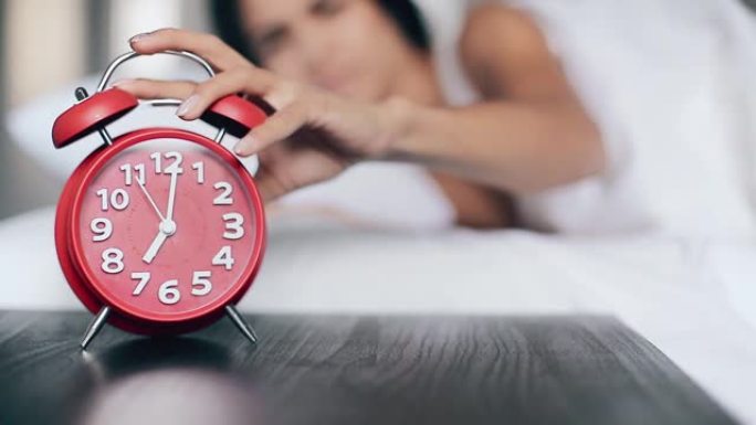 漂亮的女孩睡在床上，关掉闹钟，一直睡觉。关注闹钟