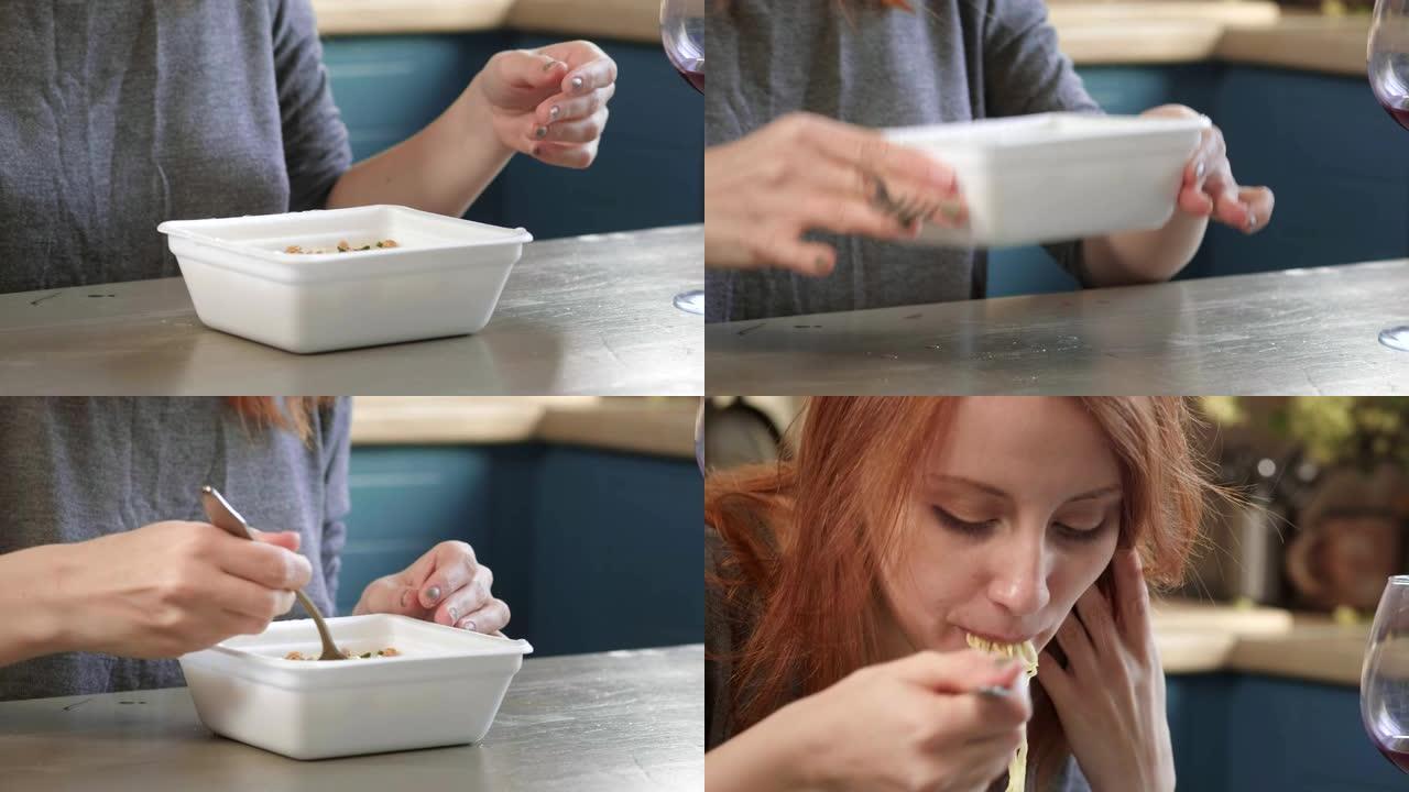 迷人的红发女孩在厨房里用叉子吃方便面。从塑料盒里吃垃圾食品。糟糕的生活方式。旅途中食物。女人从外卖盒