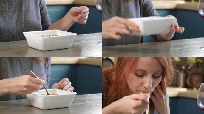 迷人的红发女孩在厨房里用叉子吃方便面。从塑料盒里吃垃圾食品。糟糕的生活方式。旅途中食物。女人从外卖盒