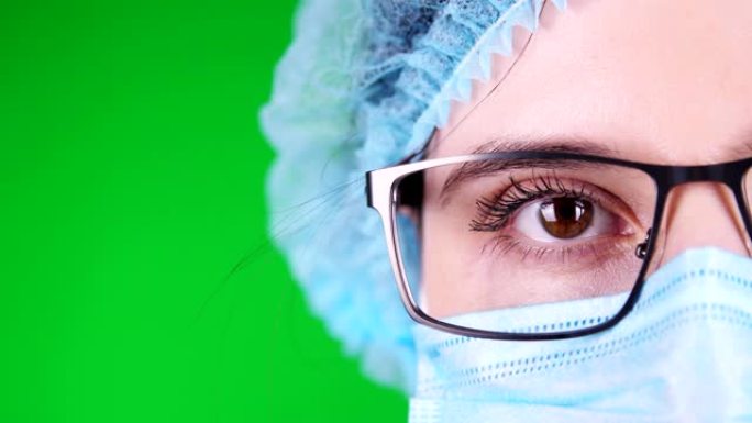 绿色背景。特写镜头，眼睛，部分戴着眼镜的女医生脸，戴着蓝色医用口罩和医用帽子