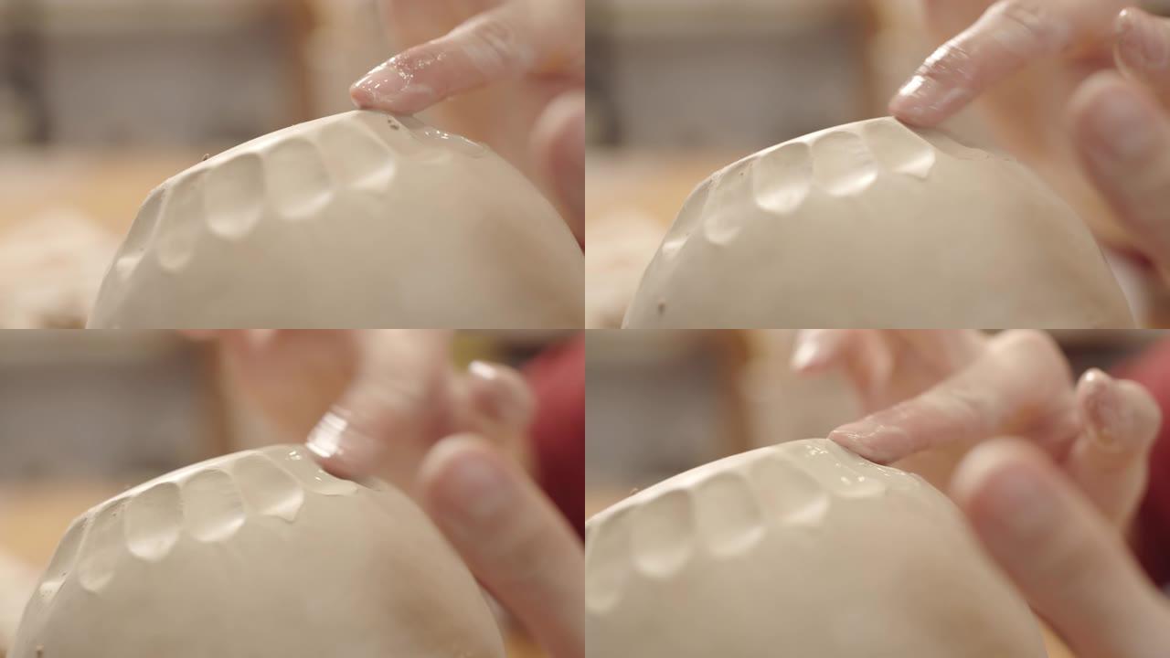 女性陶工的手在湿粘土容器上平滑切口图案