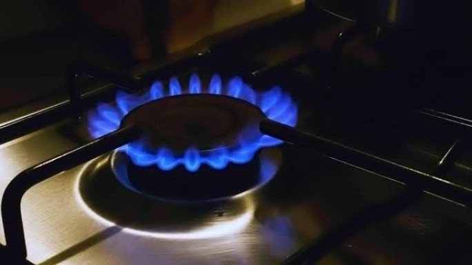 在弱光下在家用厨房中点亮的炉子的蓝色火焰的特写视图