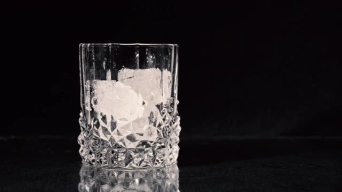 滴冰块。威士忌被倒入黑色背景的玻璃杯中。特写。